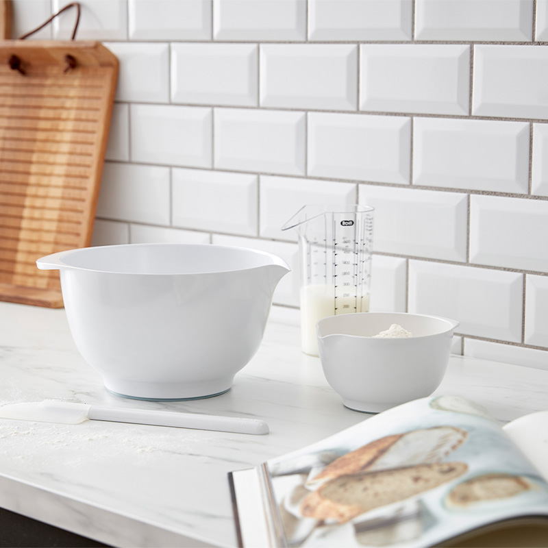 Weiße Rührschüsseln mit Messbecher auf Arbeitsplatte